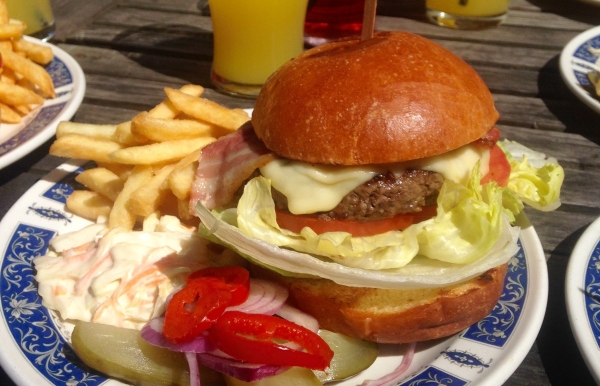 A picture of BBQ Shack's bacon cheeseburger, on a plate with chips, coleslaw, peppers, onions and gh